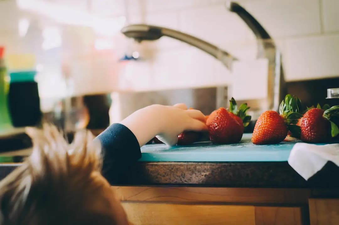 Toddler grabbing strawberries from a kitchen countertop